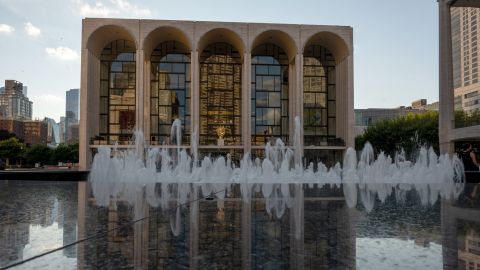 The Metropolitan Opera House is reflected off the fountain's marble enclosure in New York City.