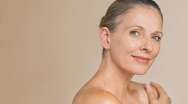 Older woman with grey hair and beautiful skin smiling at the camera.